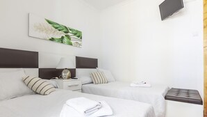 Une chambre d’hôtel avec deux lits, une télévision, une table de chevet avec une lampe et un petit pouf.