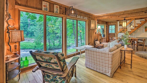 Un acogedor interior de cabaña con ventanas amplias, muebles de madera y una escalera.