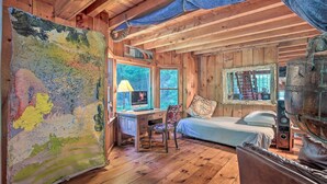Interior rústico de una cabaña con un escritorio de madera, una cama y un cuadro abstracto grande.