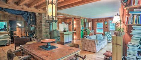 A rustic wooden interior with a dining table, chairs, a sofa, and a bookshelf.
