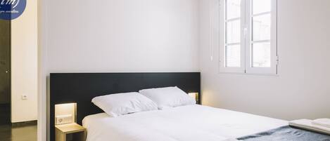 A neatly made bed with white linens, a dark headboard, and a bedside table with a lamp.