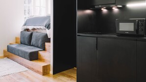 A modern kitchen with black cabinets, a microwave, and a staircase leading to a sleeping area. - ORM- Saraiva de Carvalho apartments (Porto)