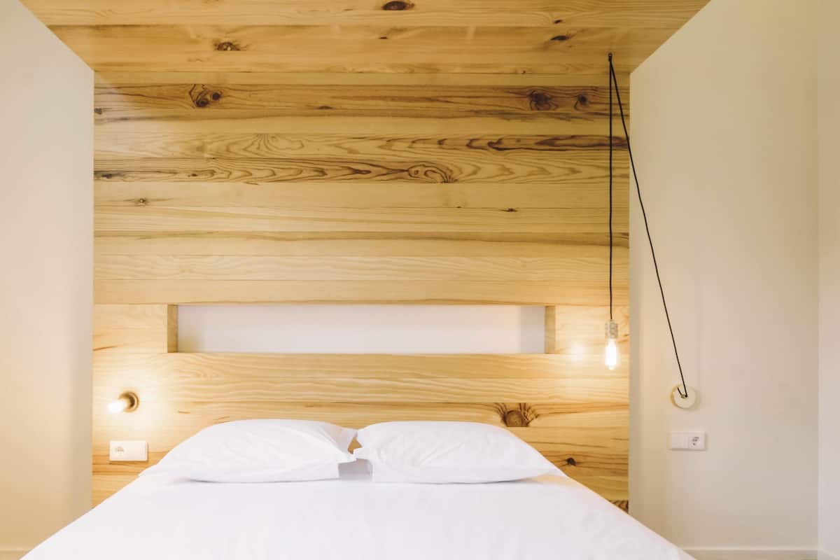 Um quarto com cabeceira de madeira, cama com roupa de cama branca e uma luminária de cabeceira.