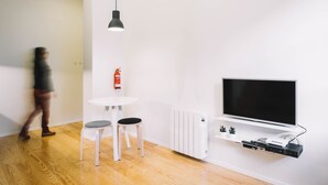 A modern living room with a flat-screen TV mounted on the wall, a white table with two chairs, and a black pendant light. - ORM- Saraiva de Carvalho apartments (Porto)