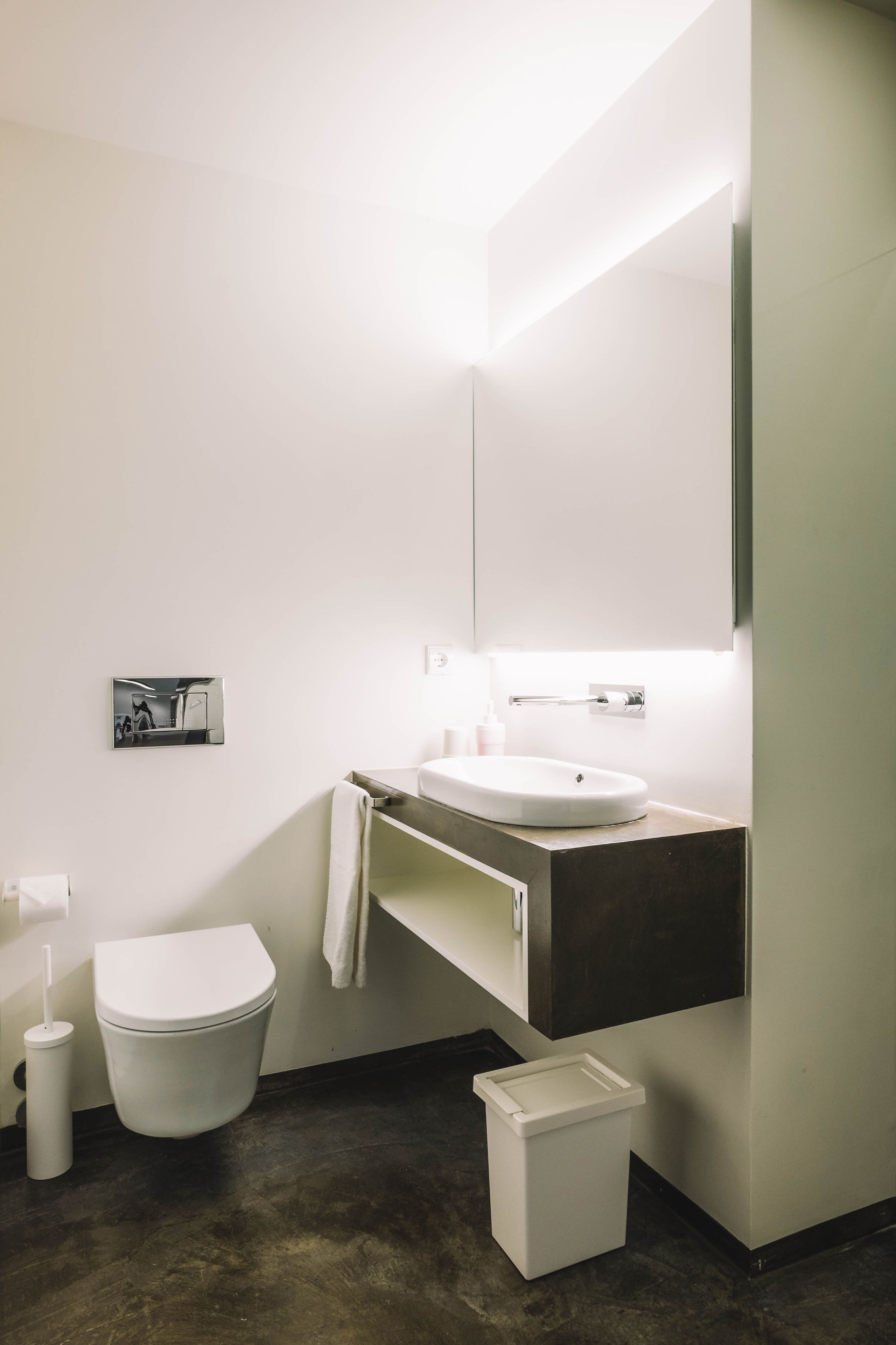 A modern bathroom with a white toilet, a sink with a dark countertop, and a mirror above the sink.