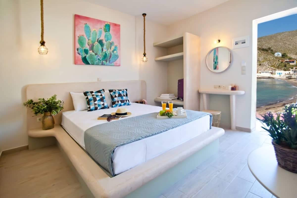 A bedroom with a large bed, bedside plants, a cactus painting, and a view of the sea.