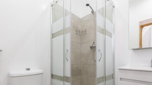 Une salle de bain moderne avec une douche à parois de verre, des toilettes blanches et un lavabo surmonté d’un miroir.