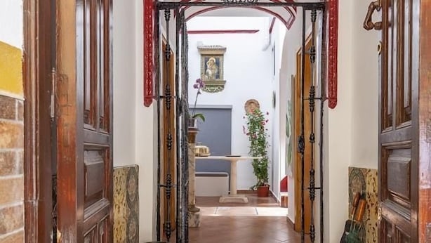 Un couloir étroit, avec des portes en bois et un sol carrelé, qui mène à une pièce comprenant un lit et une fenêtre.