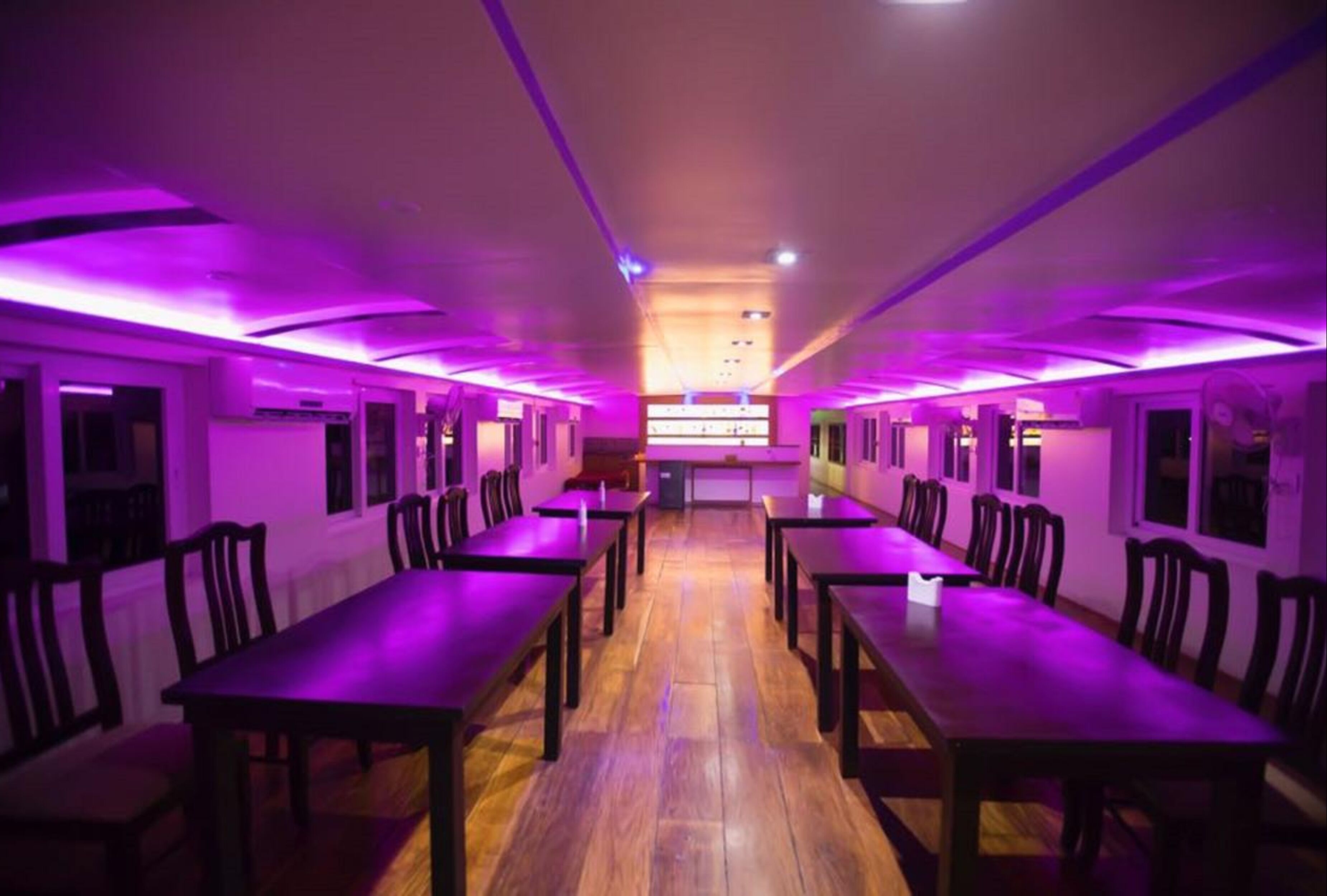 A room with multiple tables and chairs arranged in rows, with purple lighting.