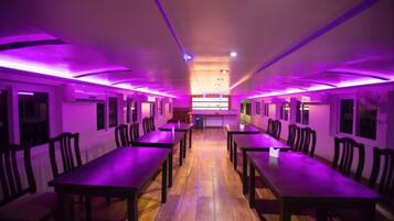 A room with multiple tables and chairs arranged in rows, with purple lighting.