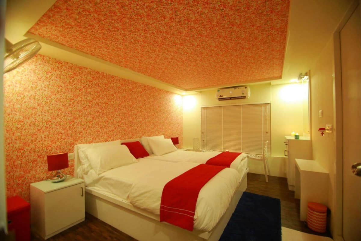 A bedroom with a bed, nightstand, lamp, and a window with blinds.