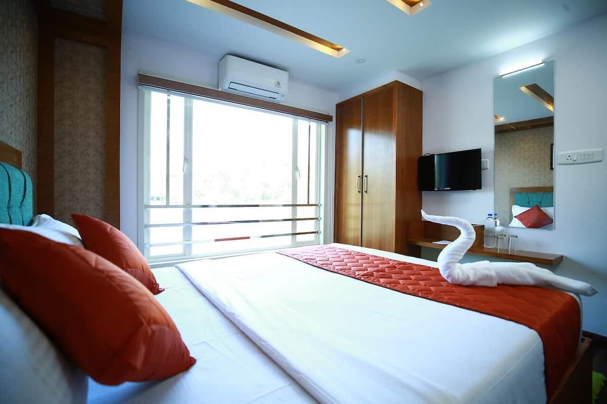 A hotel room with a large bed, a TV, a wardrobe, and a window with blinds.