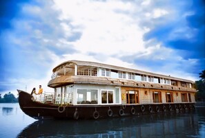 Una amplia casa flotante de varios niveles, con una cubierta superior protegida y una cubierta inferior con ventanas.