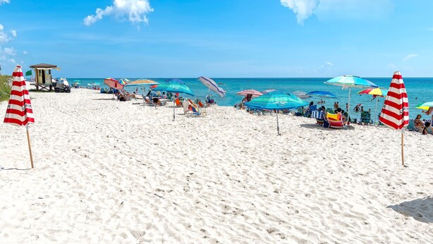 Ein Strand mit Sonnenschirmen, Liegestühlen und einem Rettungsturm.