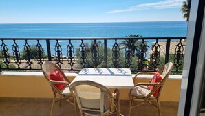 A balcony with wicker chairs and a table, overlooking a coastal view with the sea and palm trees. - Corfu Island Apartment 40 (Corfu)
