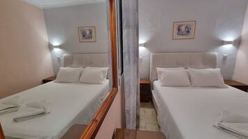A hotel room with two single beds, each with a wooden headboard, white bedding, and a nightstand. There are wall-mounted lights above each bed and a framed picture on the wall.