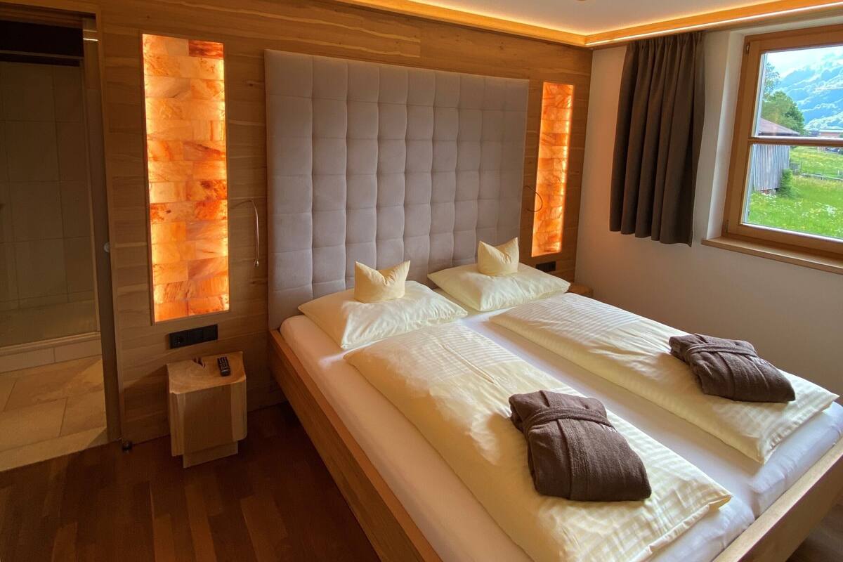 A large bed with a tufted headboard, two pillows, and two towels.