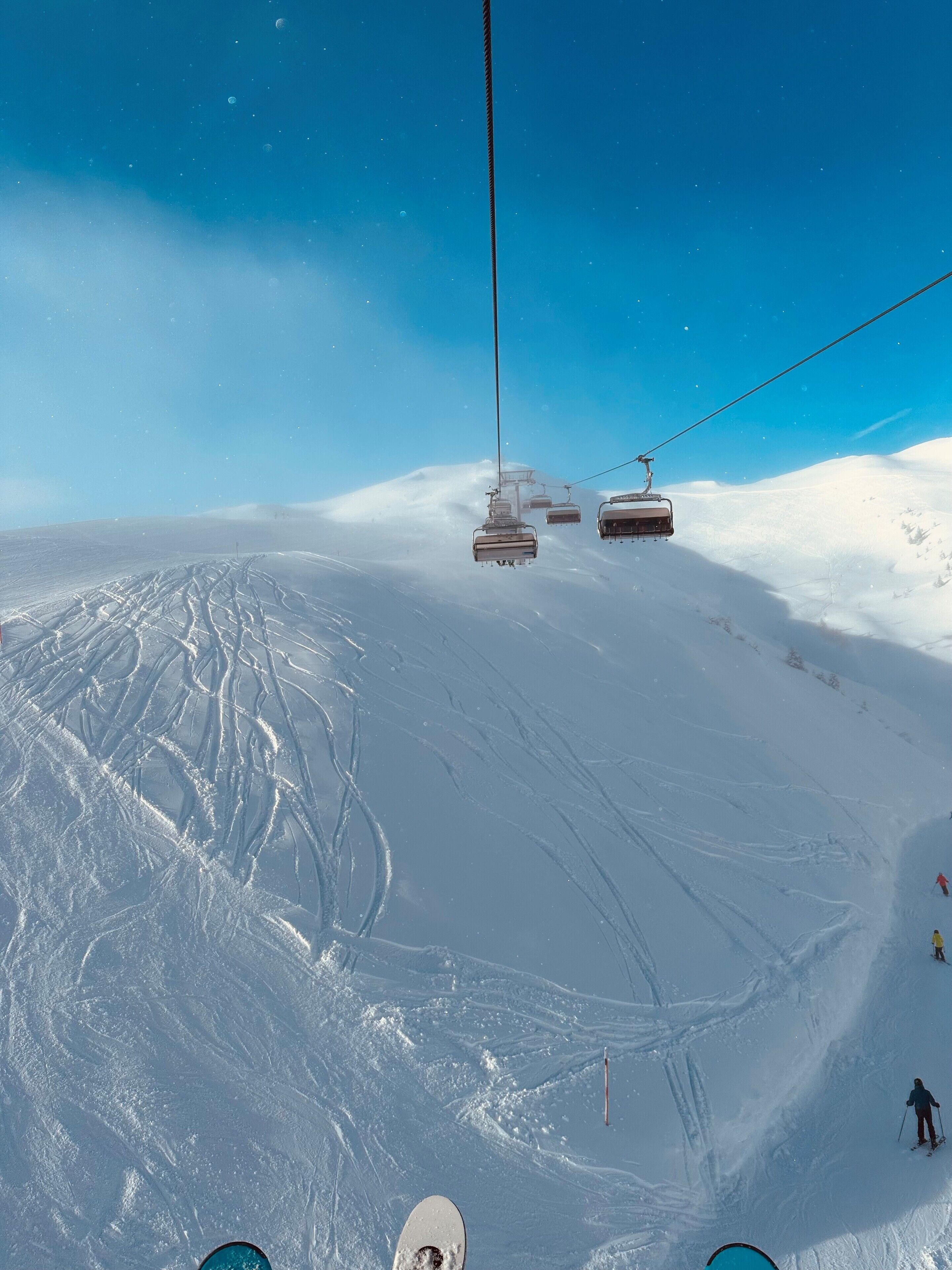 A ski lift with chairs moving over a snowy slope.