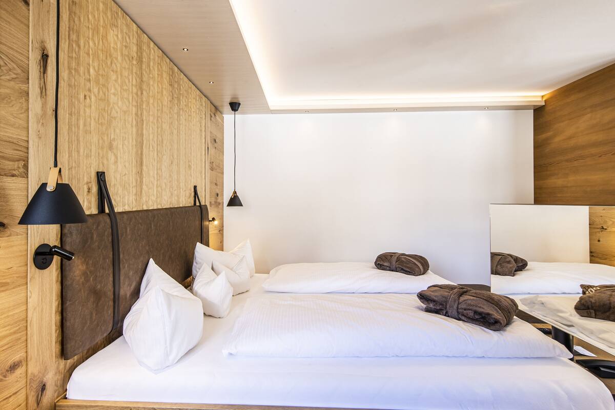 A modern hotel room with wooden walls, a large bed with white linens, two bedside lamps, and a wooden headboard.