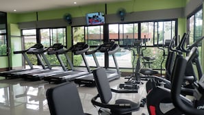 Een sportschool met loopbanden, trainingsfietsen en een televisiescherm.