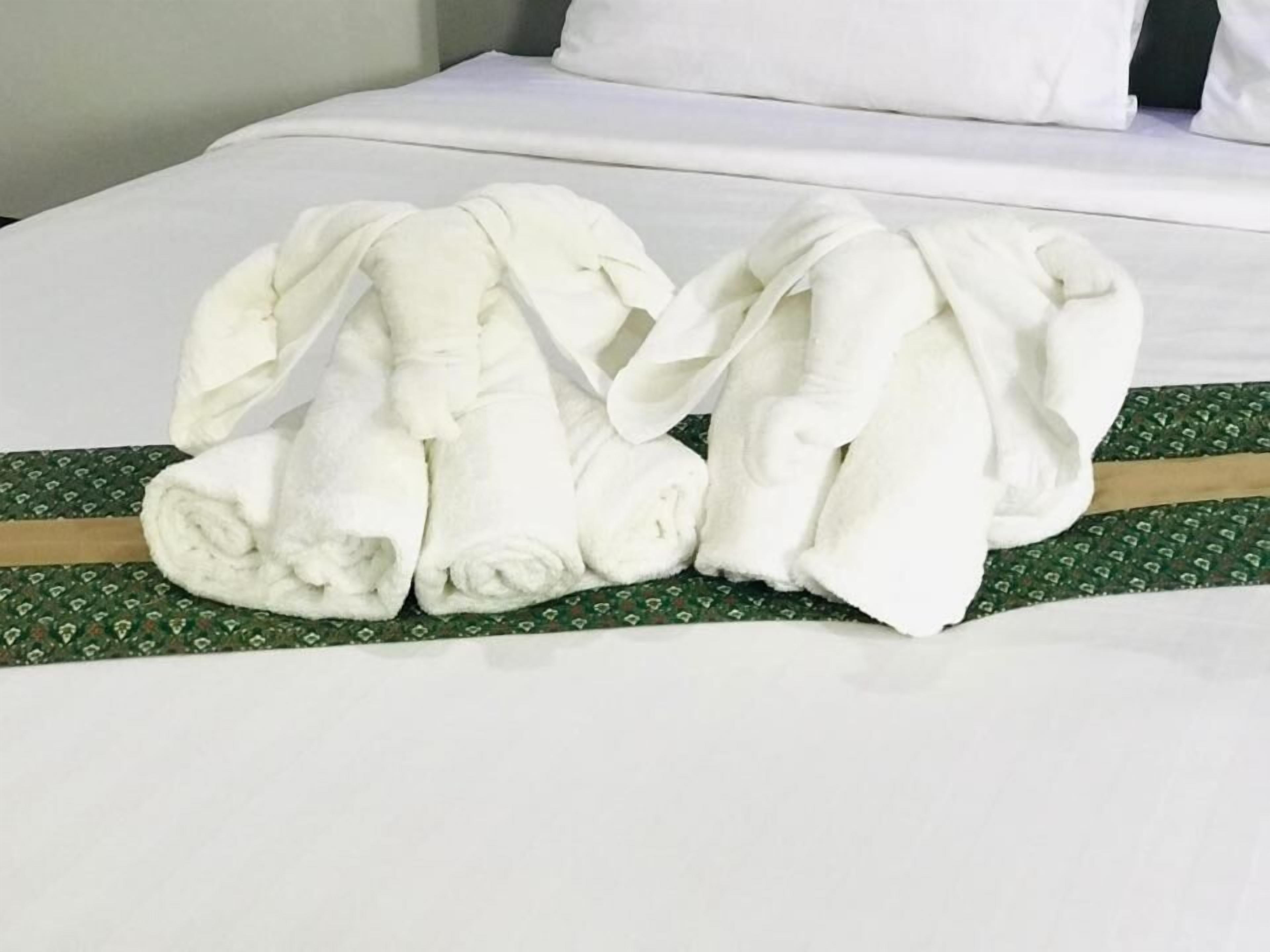 Un lit bien fait, avec du linge de lit blanc et un couvre-lit vert à motifs.