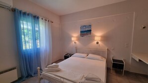 Quarto com cama, mesa de cabeceira, luminária na parede e janela com cortinas.