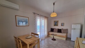 Um espaço compacto com mesa de jantar, cadeiras, sofá, uma mesinha, frigorífico e ventoinha no teto.