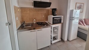 Uma cozinha compacta com armários brancos, micro-ondas, cafeteira e geladeira.