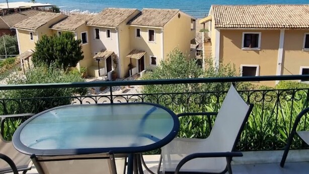 Varanda com mesa e cadeiras de vidro, com vista para a costa, edifícios e o mar.