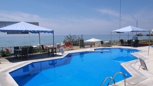Ein Pool mit Blick auf das Meer, umgeben von Liegestühlen und Sonnenschirmen.