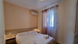 Ein Hotelzimmer mit Bett, Nachttisch, Klimaanlage und Fenster mit leichtem Vorhang.