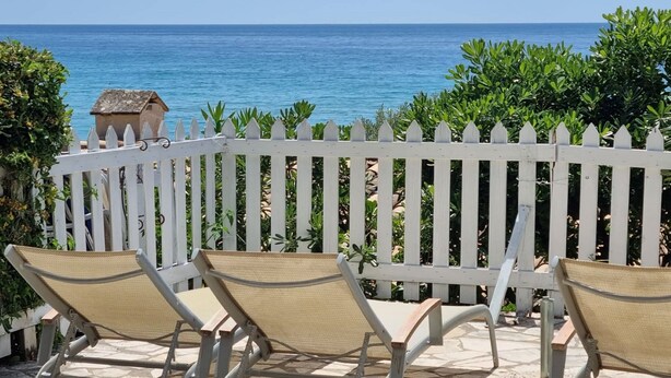 Eine Terrasse mit zwei Stühlen und einem weißen Zaun, mit Blick auf das Meer.