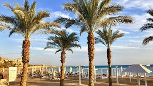 A beach with palm trees, sun loungers, and umbrellas. - Luxury villa with sea view and pool (Hurghada)