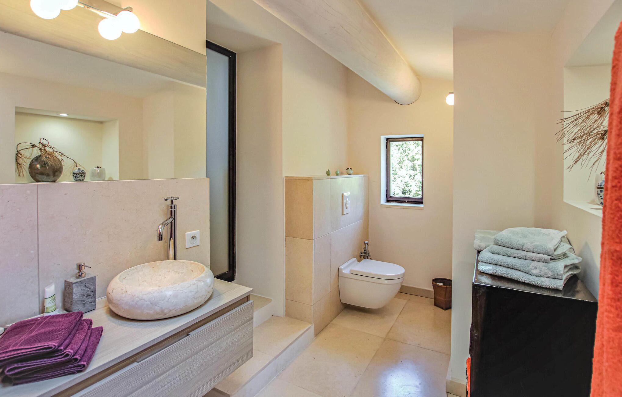 Une salle de bain moderne avec un lavabo rond, des toilettes et une fenêtre.
