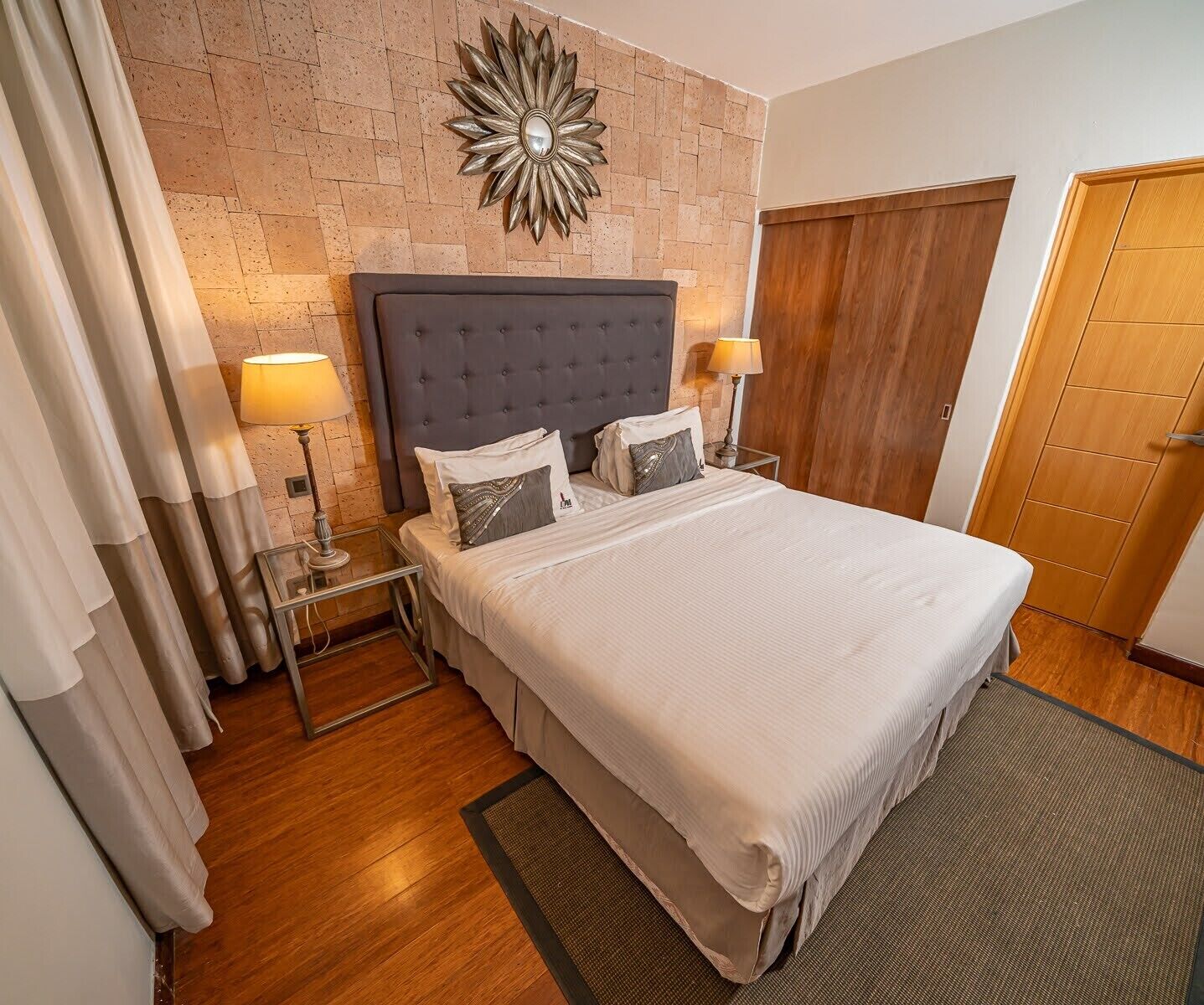 A hotel room with a large bed, two bedside lamps, a decorative wall piece, and a wooden door.