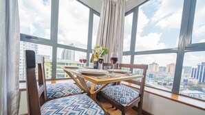 Een eethoek met een tafel voor twee personen, een stadszicht door grote ramen en gestreepte kussens op de stoelen.