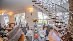 Een moderne woonkamer met een eethoek, een spiltrap en grote ramen.