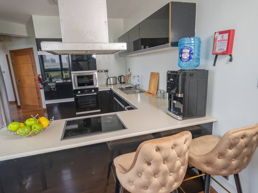Una cocina moderna con una isla central, dos taburetes de bar, una cafetera y un dispensador de agua.