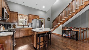 A kitchen with wooden cabinets, a stainless steel refrigerator, a granite countertop, and a wooden staircase with holiday decorations. - Pool&SplashPad Hot Tub PoolTable, Foosball, Lake, Shows, Golf, Shop, FUN (Hollister)