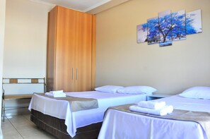 A hotel room with two beds, a wooden wardrobe, and a bench.
