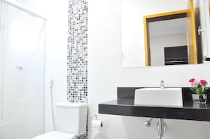 A modern bathroom with a glass shower enclosure, a toilet, a sink with a black countertop, and a mirror with a wooden frame.