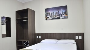 Una habitación de hotel con una cama, un armario, un cuadro de un paisaje urbano en la pared y un espejo.