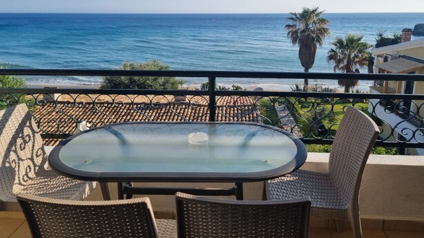 A balcony with a glass table and wicker chairs, overlooking a coastal view with palm trees and a clear sky. - Corfu Island Apartment 23 (Corfu)