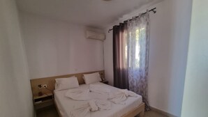 A single bed with a wooden frame, a nightstand, a power outlet, and a window with curtains. - Corfu Island Apartment 23 (Corfu)