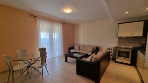 A modern living room with a sofa, coffee table, and dining area with chairs. There is a kitchen with an oven and cabinets. - Corfu Island Apartment 23 (Corfu)