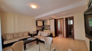 A modern living room with a sofa, chairs, a coffee table, and a glass dining table. There is a kitchen area with cabinets and a microwave. - Corfu Island Apartment 23 (Corfu)