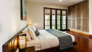 A neatly made bed with pillows and a blanket, a bedside lamp, and a window with wooden shutters. - Karma Luxury 2 bd. VILLA *TOP 5 stars BALi RESORT* (Ungasan)