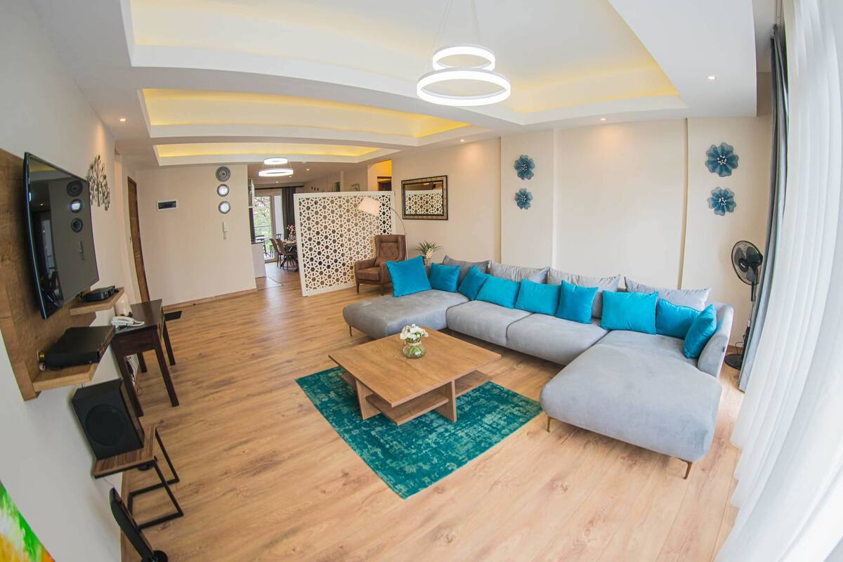 Een moderne woonkamer met een grijze modulaire bank, een houten salontafel en een groen tapijt.