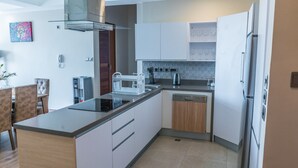 A modern kitchen with a central island, built-in dishwasher, and white cabinetry.