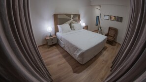 Une chambre à coucher avec un grand lit, une table de chevet avec une lampe, une chaise et un miroir au mur.